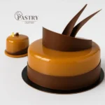 A refined French dessert featuring layers of cinnamon madeleine sponge, creamy milk chocolate-coffee crémeux, smooth white coffee mousse, and a delicate mirror glaze.