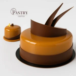 A refined French dessert featuring layers of cinnamon madeleine sponge, creamy milk chocolate-coffee crémeux, smooth white coffee mousse, and a delicate mirror glaze.